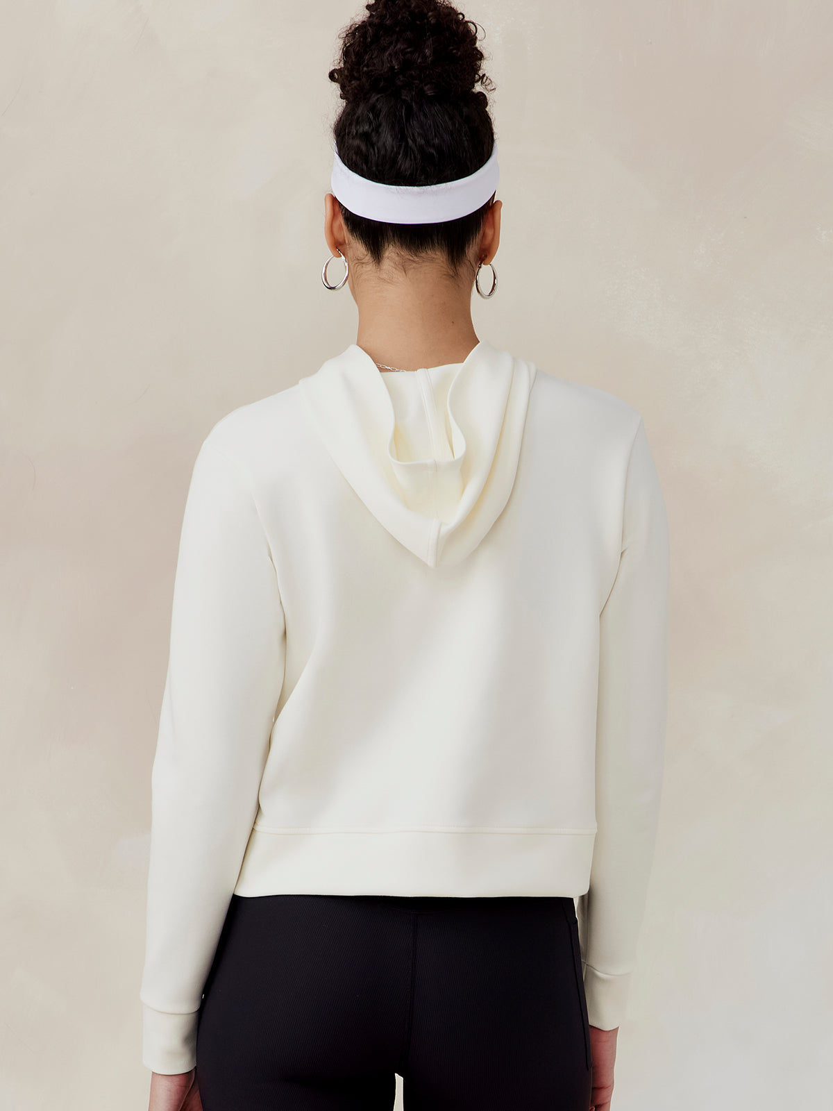 Woman wearing a white Highlands Hoodie with a hood, shown from the back, paired with black pants and a white headband tasc Highlands Hoodie (Coconut)