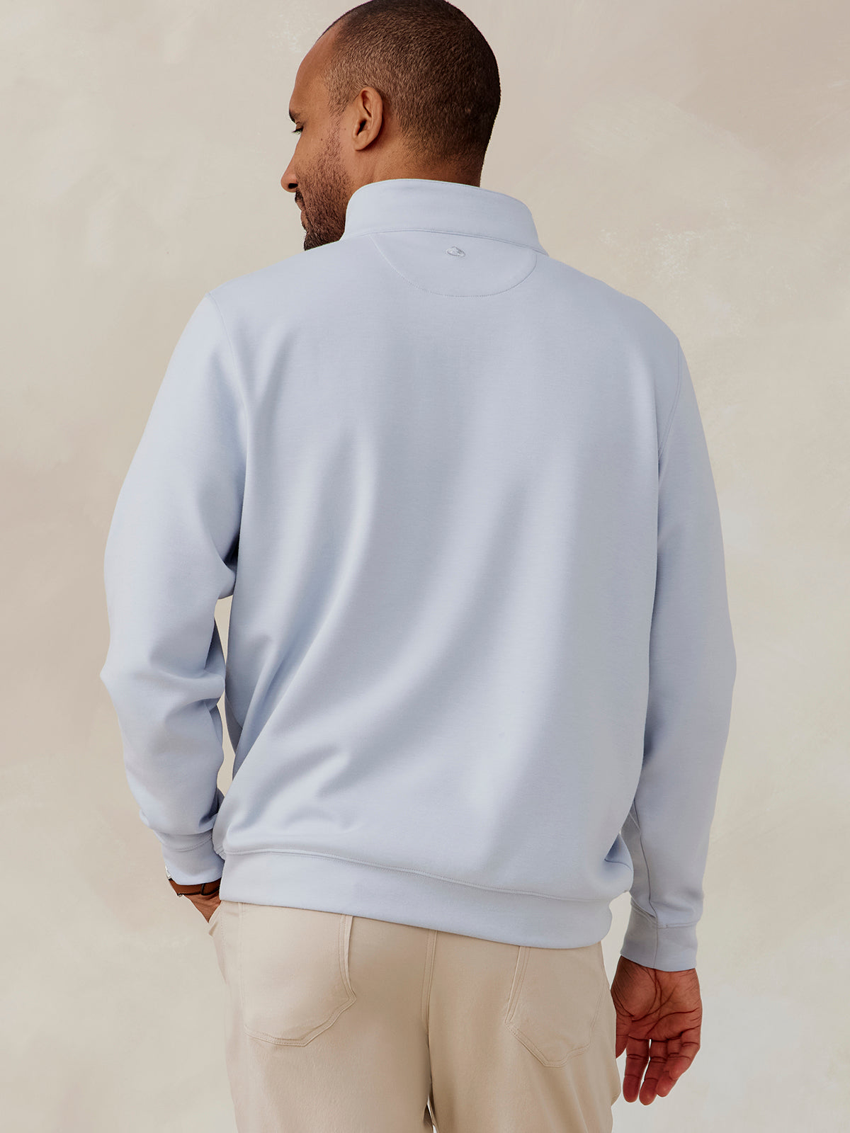 Man wearing light blue Highlands quarter zip pullover with long sleeves, standing facing away, paired with beige pants tasc Highlands Quarter Zip (Cloud)