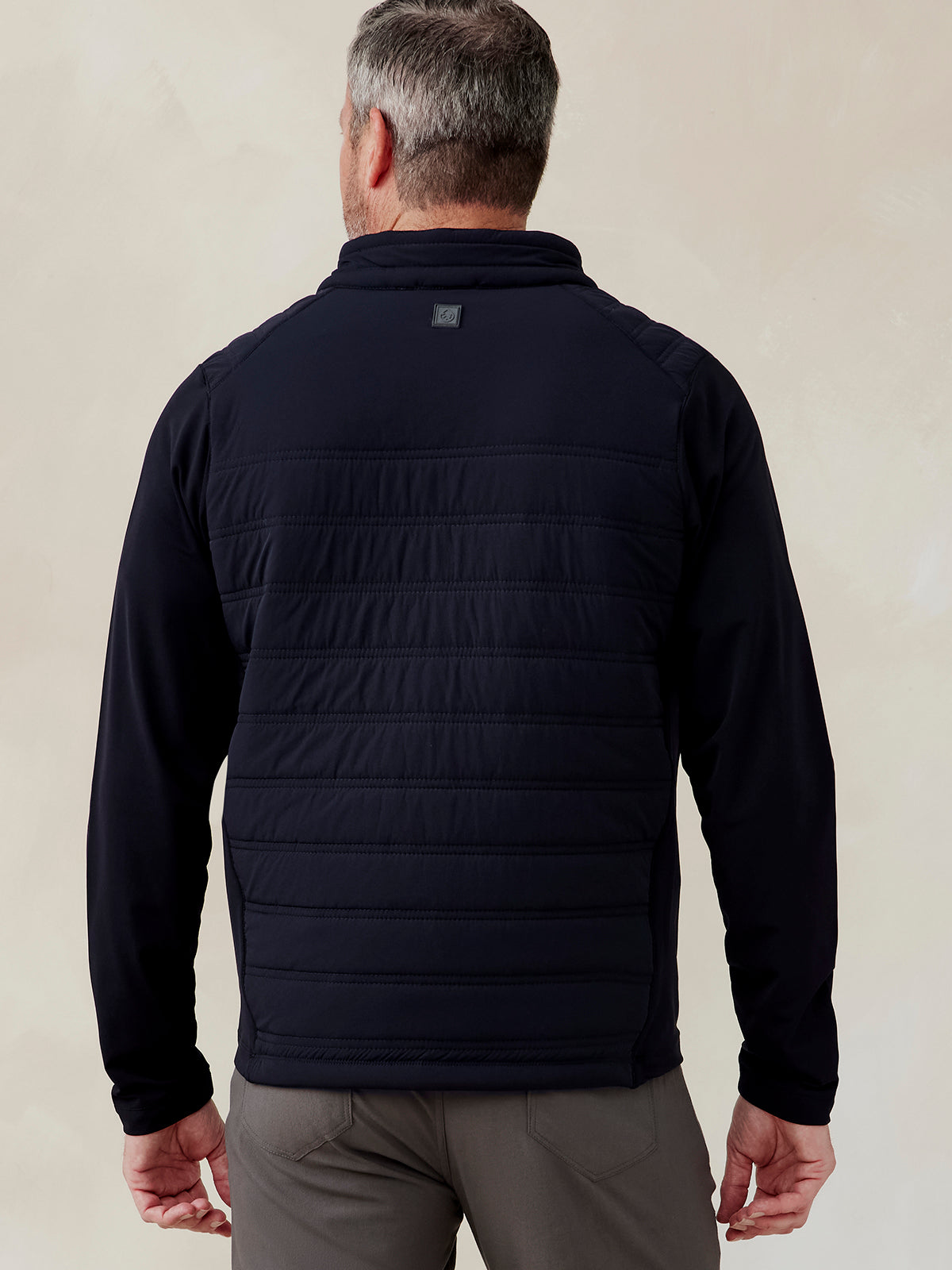 Man wearing a black Hilltop Hybrid Jacket with quilted back panel and long sleeves, shown from the back Hilltop Hybrid Jacket (Black)