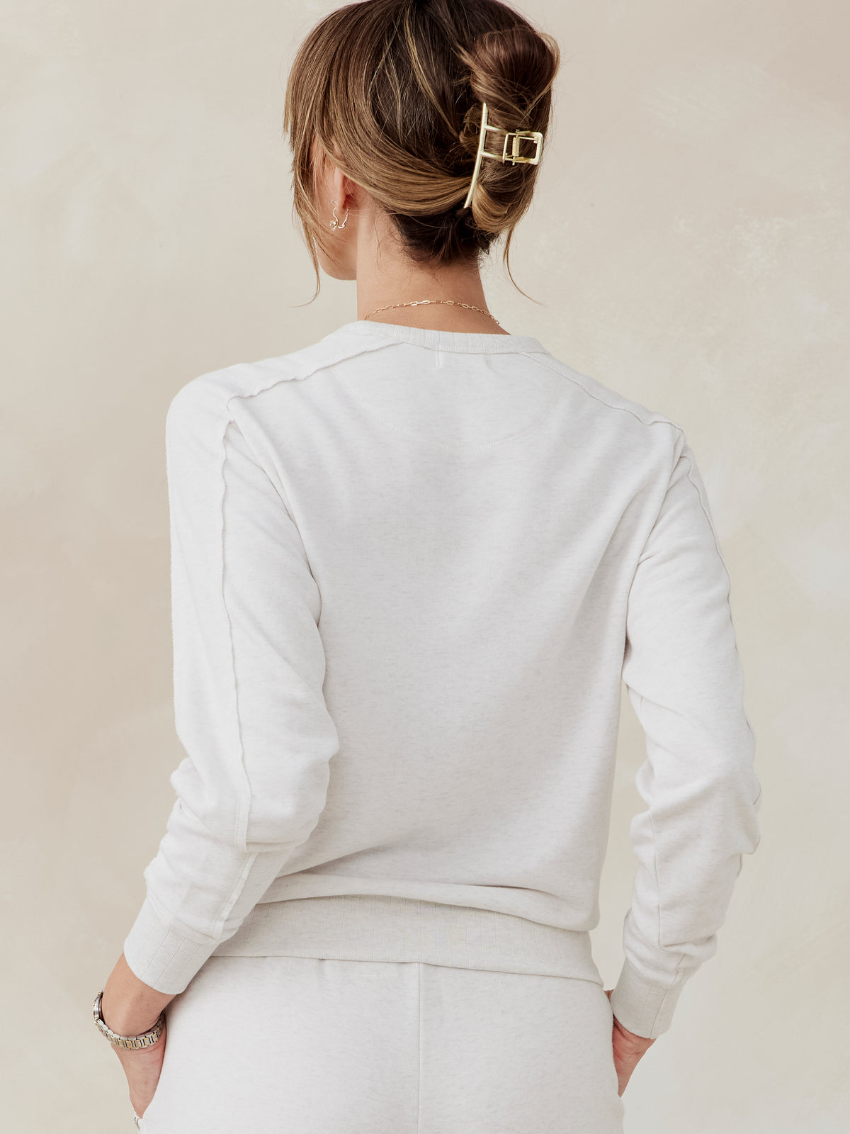 Woman wearing a light beige Stadium French Terry sweatshirt and matching pants, back view showing seam details and ribbed cuffs tasc Stadium Sweatshirt (CoconutHeather)