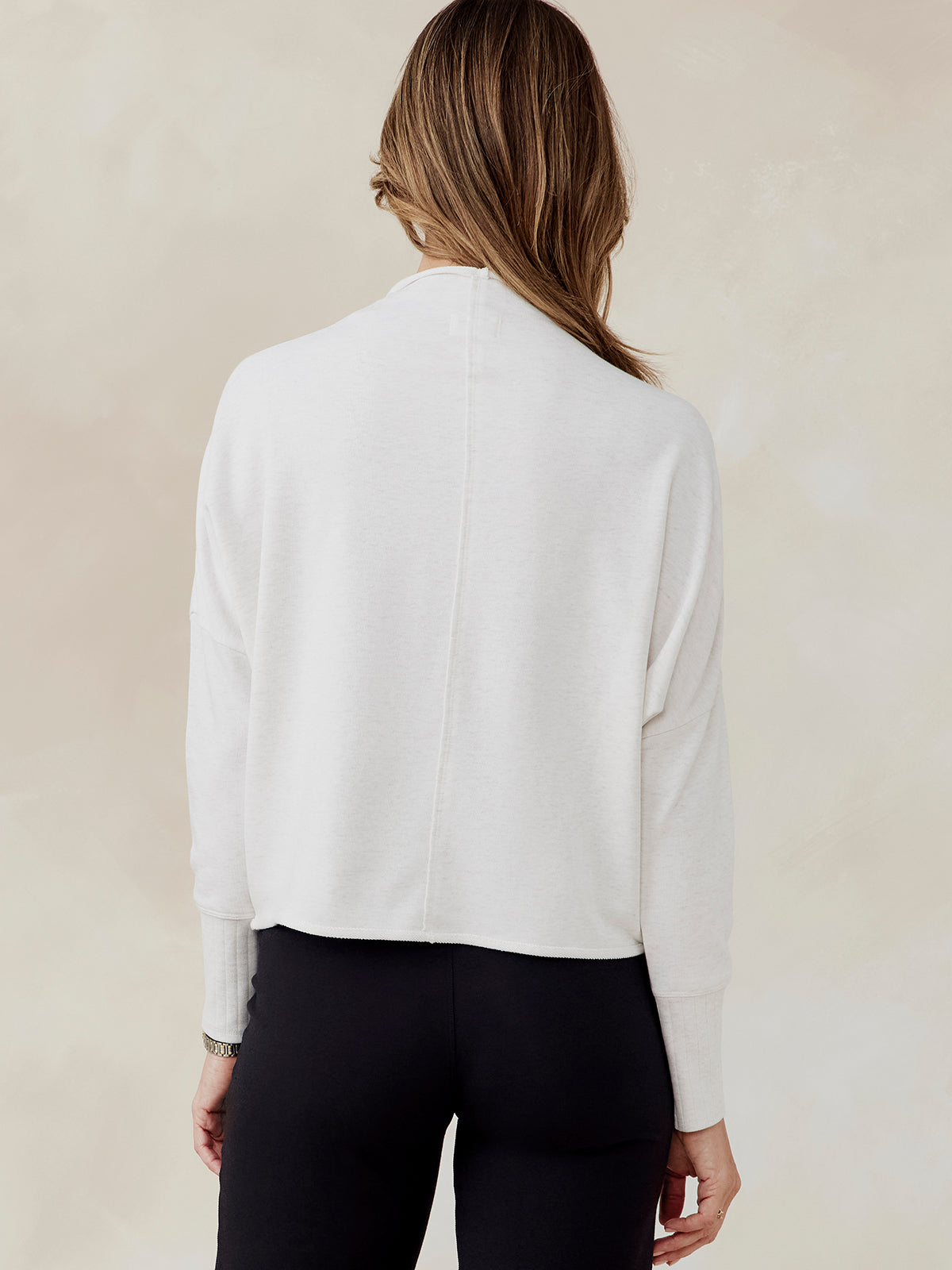 Woman wearing white French terry dolman sweatshirt with ribbed cuffs, shown from back, paired with black pants tasc Performance French Terry Dolman Sweatshirt (CoconutHeather)