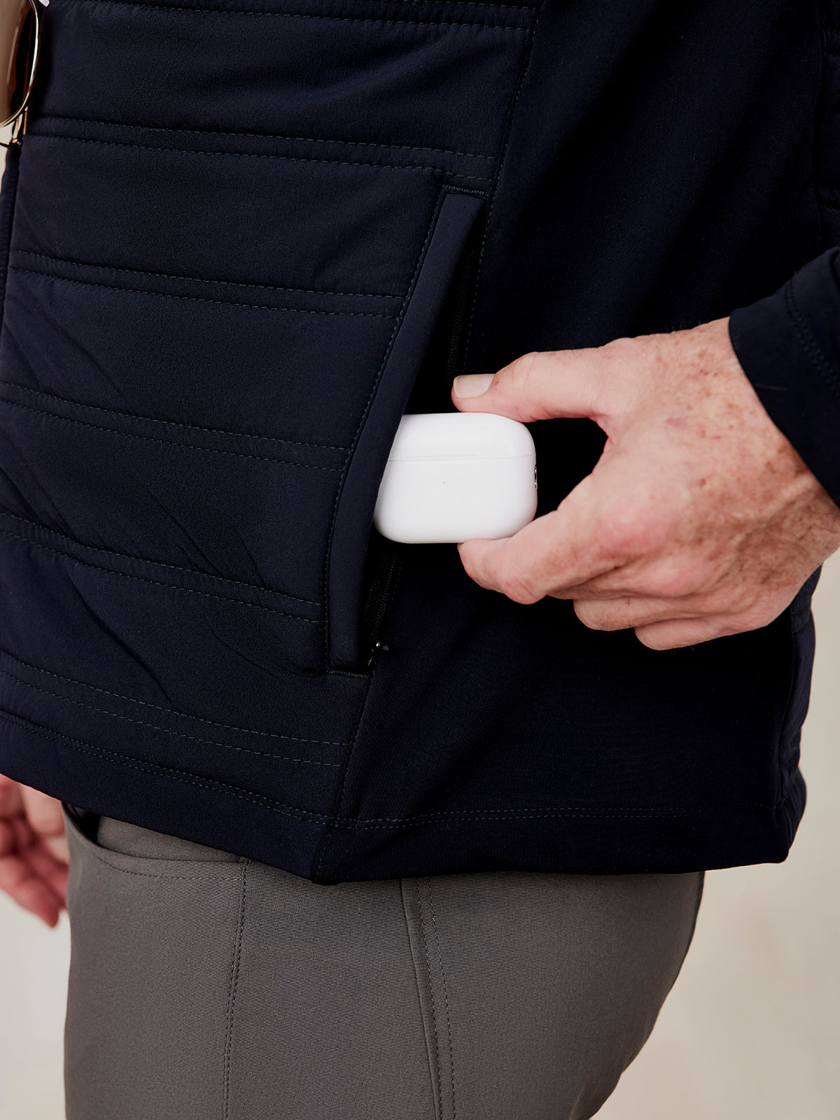 Black Hilltop Hybrid Jacket close-up showing quilted front pocket with zipper and hand placing white case inside Hilltop Hybrid Jacket (Black)