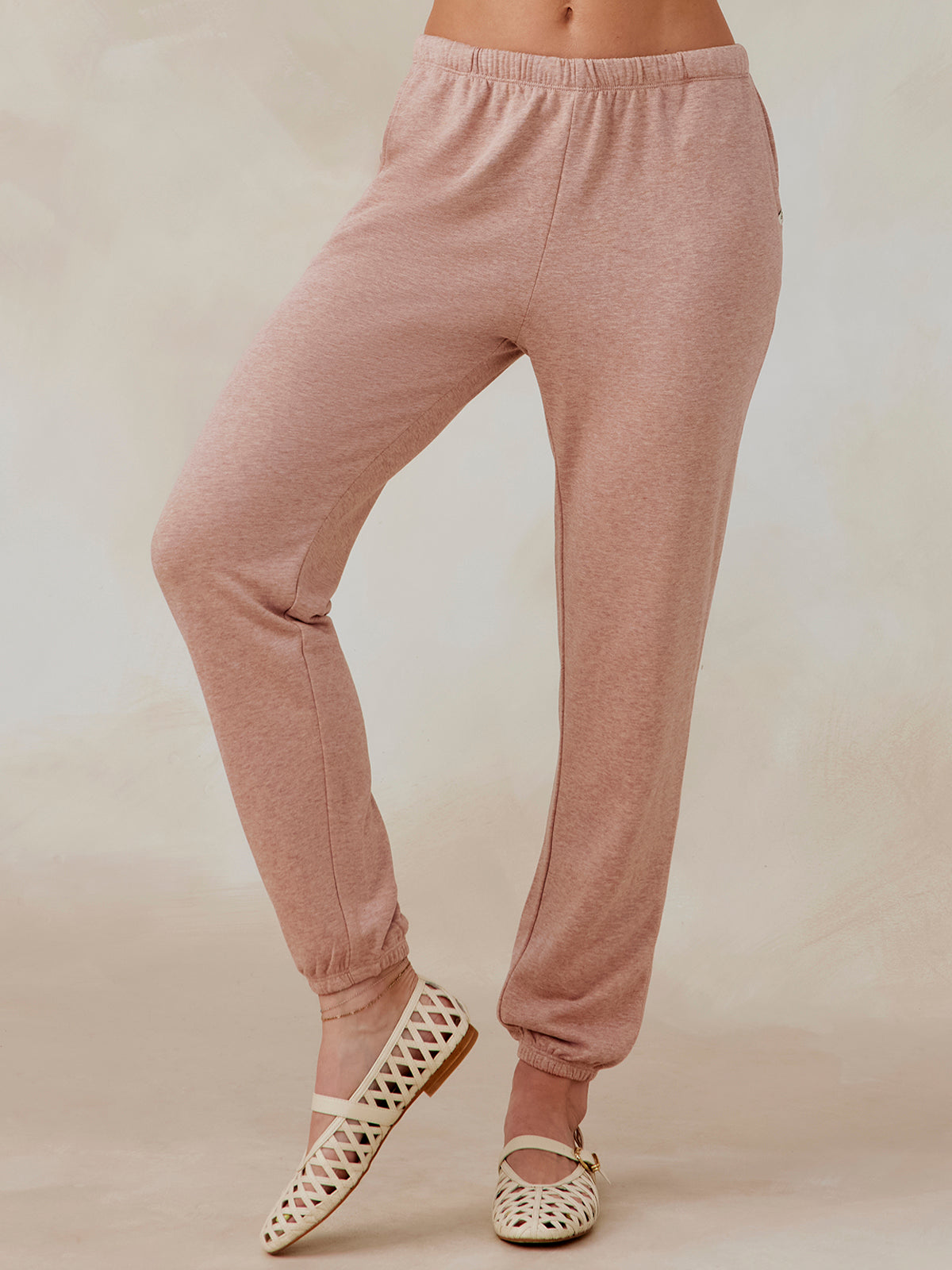 Woman wearing dusty pink Stadium French Terry sweatpants with elastic waistband and cuffs, paired with cream lattice flats tasc performance stadium sweatpant (AntiqueRosyHeather)