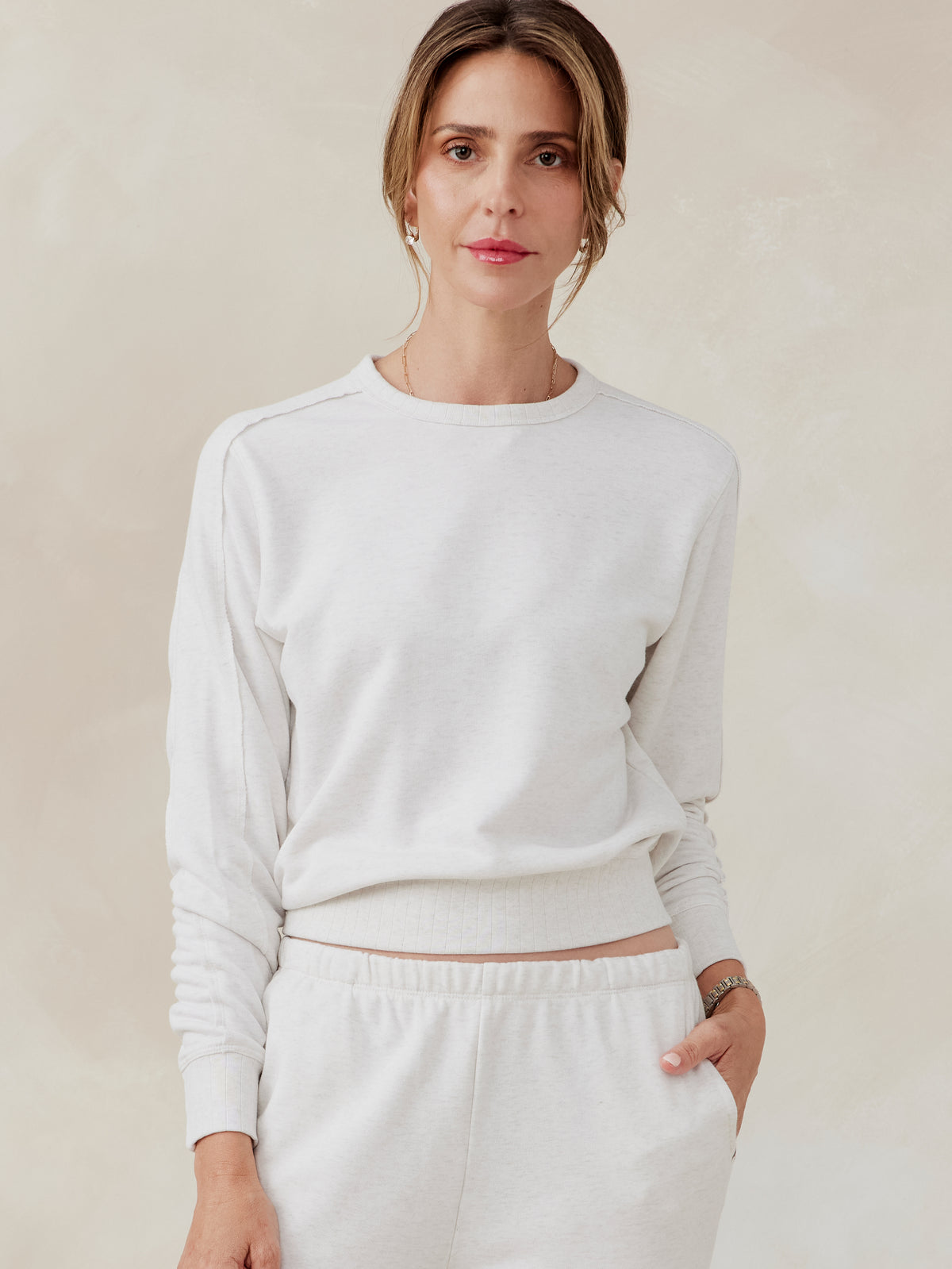 Woman wearing a white French terry sweatshirt with ribbed crew neckline and matching white sweatpants, front view tasc Stadium Sweatshirt (CoconutHeather)