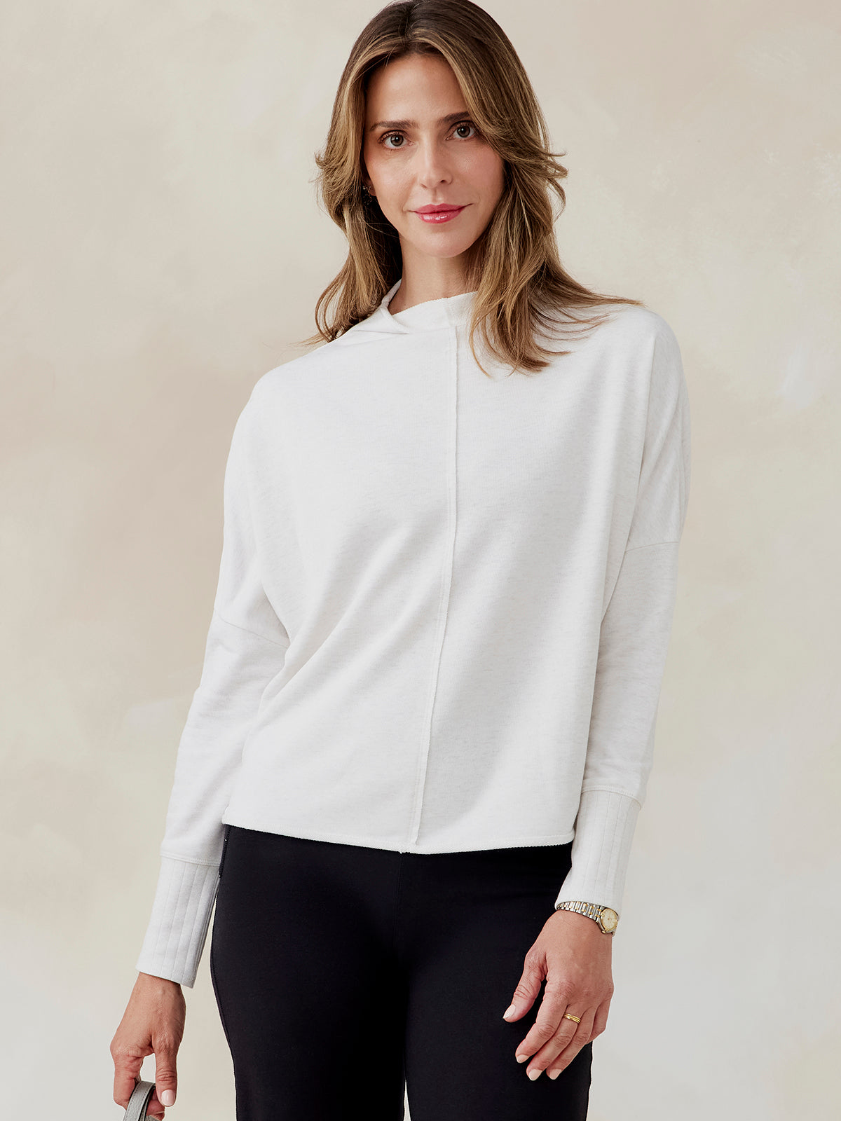 Woman wearing white French terry dolman sweatshirt with ribbed cuffs and center seam, paired with black pants, front view tasc Performance French Terry Dolman Sweatshirt (CoconutHeather)