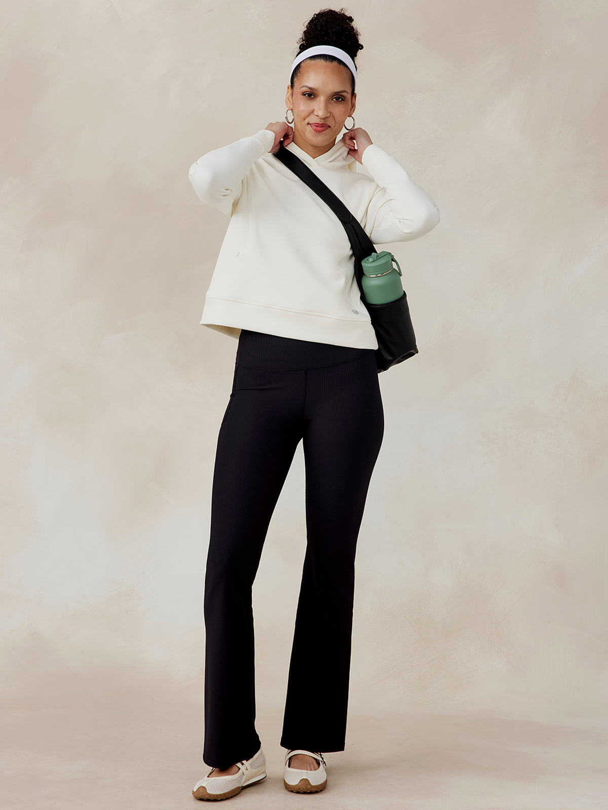 Woman wearing an off-white Highlands Hoodie with long sleeves and a hood, paired with black pants and white shoes tasc Highlands Hoodie (Coconut)