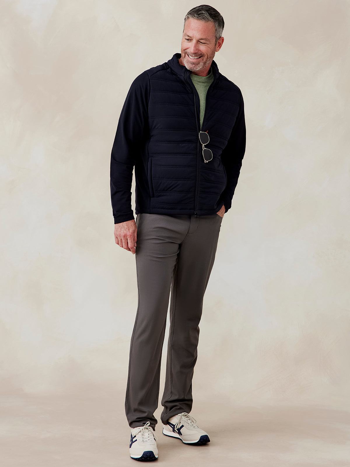 Man wearing a black Hilltop Hybrid Jacket with quilted front and zip pockets, paired with gray pants and white sneakers Hilltop Hybrid Jacket (Black)