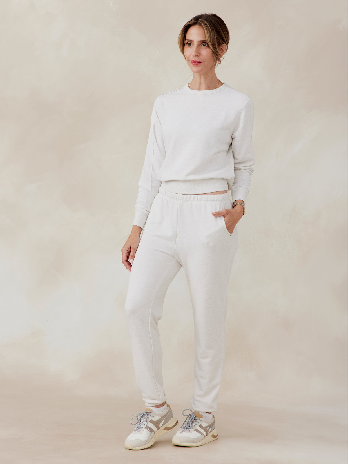 Woman wearing light beige Stadium French Terry sweatpants with elastic waistband and side pockets, paired with matching sweatshirt tasc performance stadium sweatpant (CoconutHeather)