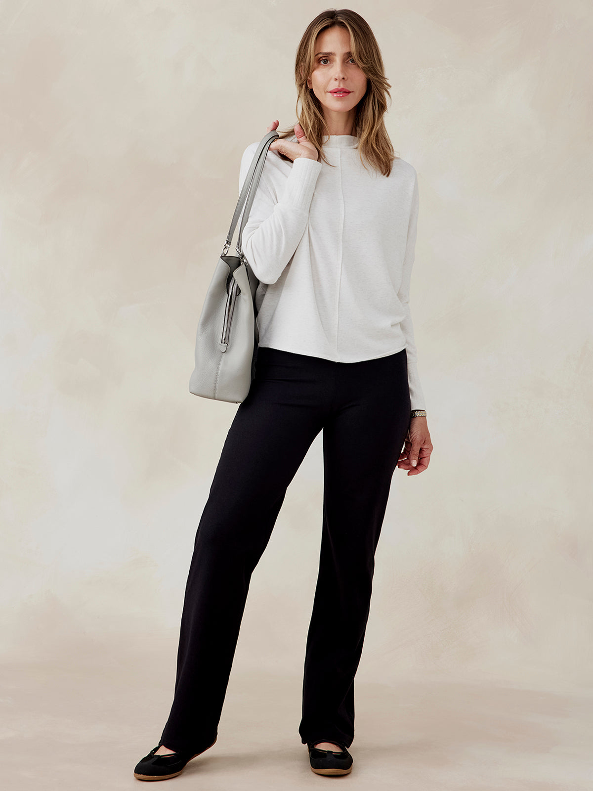 Woman wearing a light gray French terry dolman sweatshirt with long sleeves, paired with black pants and black flats tasc Performance French Terry Dolman Sweatshirt (CoconutHeather)