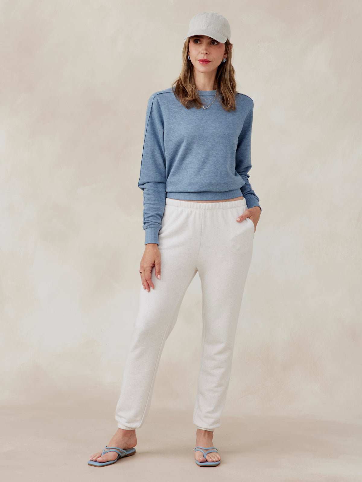 Woman wearing a blue Stadium French Terry sweatshirt with ribbed cuffs and hem, paired with white sweatpants and a beige cap tasc Stadium Sweatshirt (AnchorHeather)