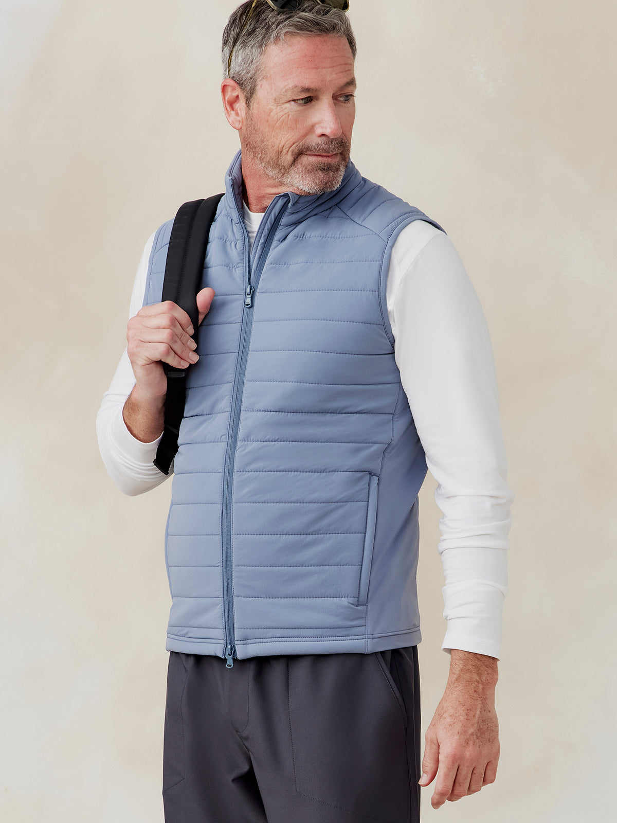 Man wearing a light blue quilted Hilltop Hybrid Vest with front zipper and side pockets over a white long-sleeve shirt tasc Hilltop Hybrid Vest (Anchor)