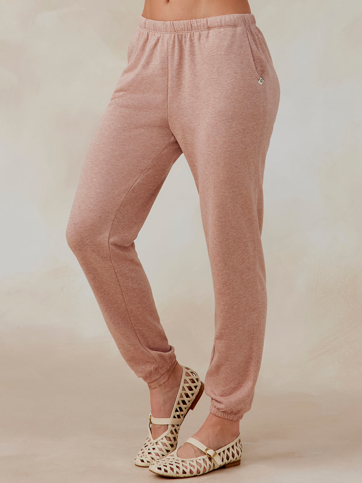 Woman wearing dusty pink Stadium French Terry sweatpants with elastic waistband and ankle cuffs, side pockets visible tasc performance stadium sweatpant (AntiqueRosyHeather)