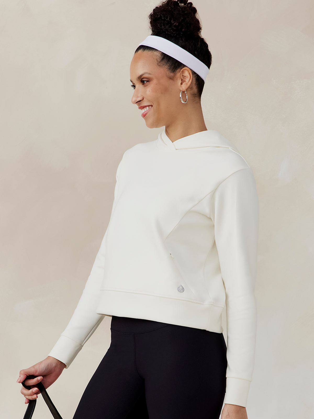Woman wearing a white Highlands hoodie with long sleeves and a hood, paired with black leggings, side view tasc Highlands Hoodie (Coconut)