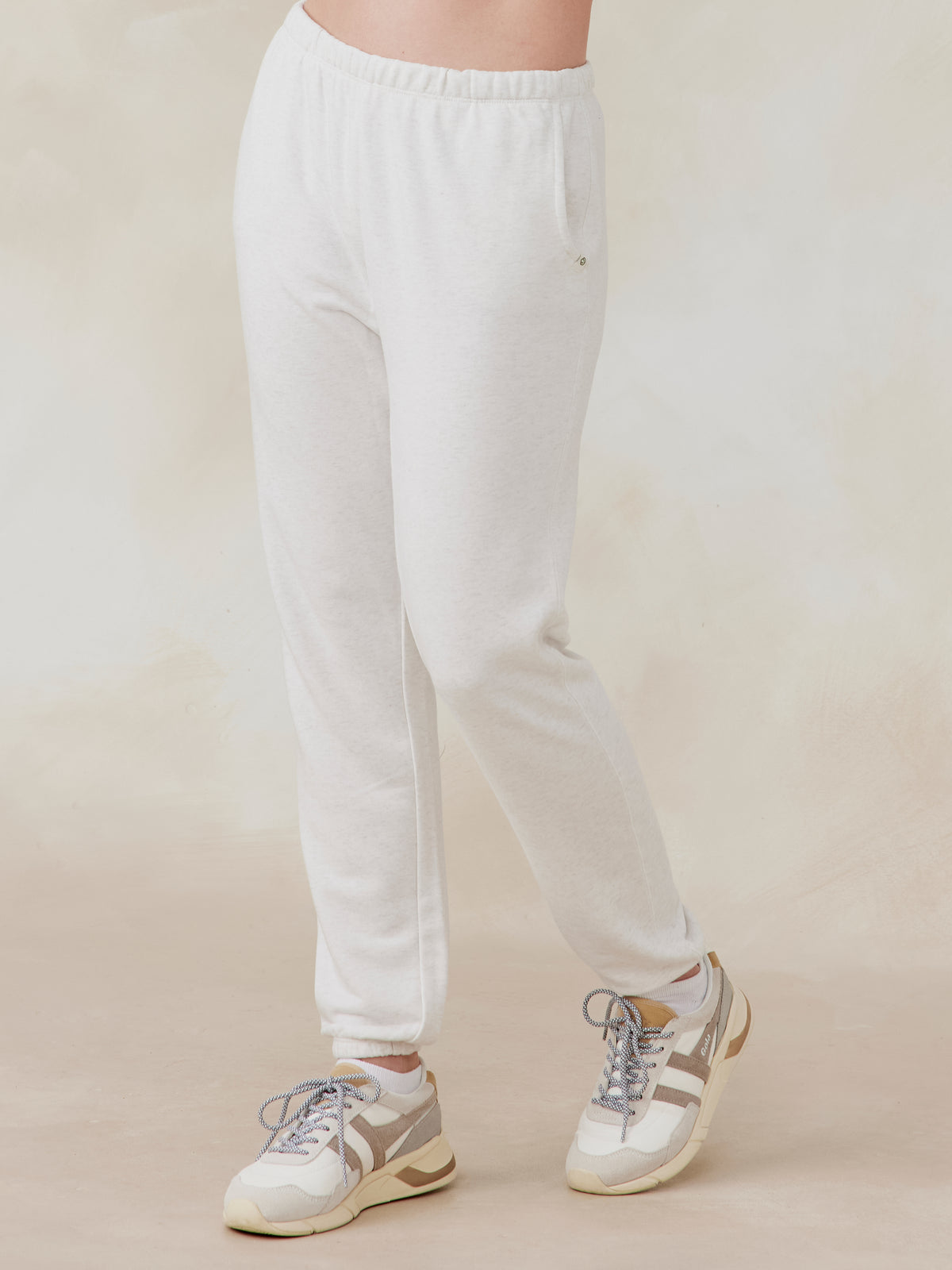 Off-white French terry sweatpants with elastic waistband and side pockets, worn by model with sneakers, front side view tasc performance stadium sweatpant (CoconutHeather)