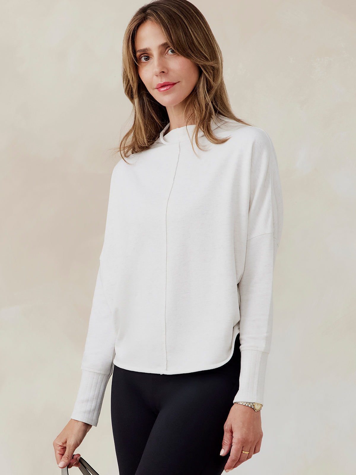 Woman wearing white French terry dolman sweatshirt with ribbed cuffs and center seam, paired with black leggings, front view tasc Performance French Terry Dolman Sweatshirt (CoconutHeather)