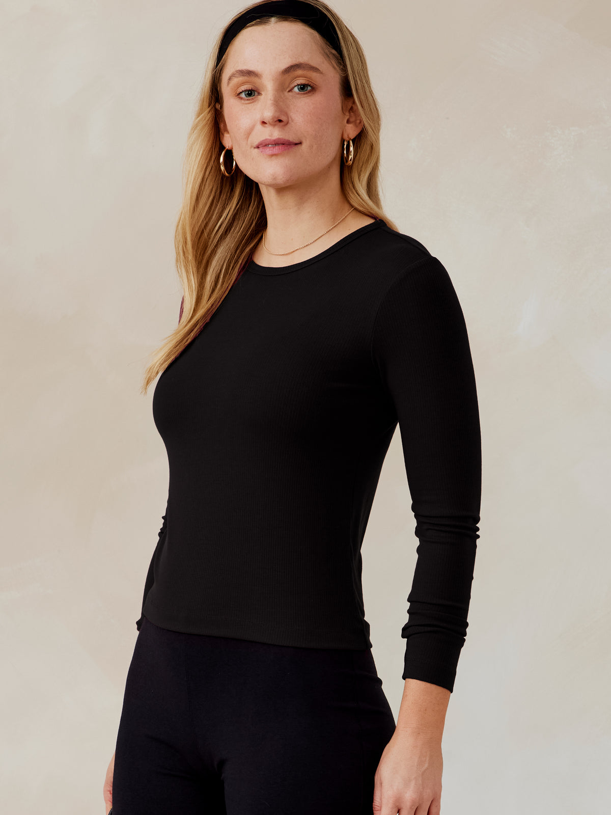 Woman wearing a black Microluxe rib long sleeve top with crew neckline, paired with black pants, front side view tasc Microluxe Rib LS (Black)